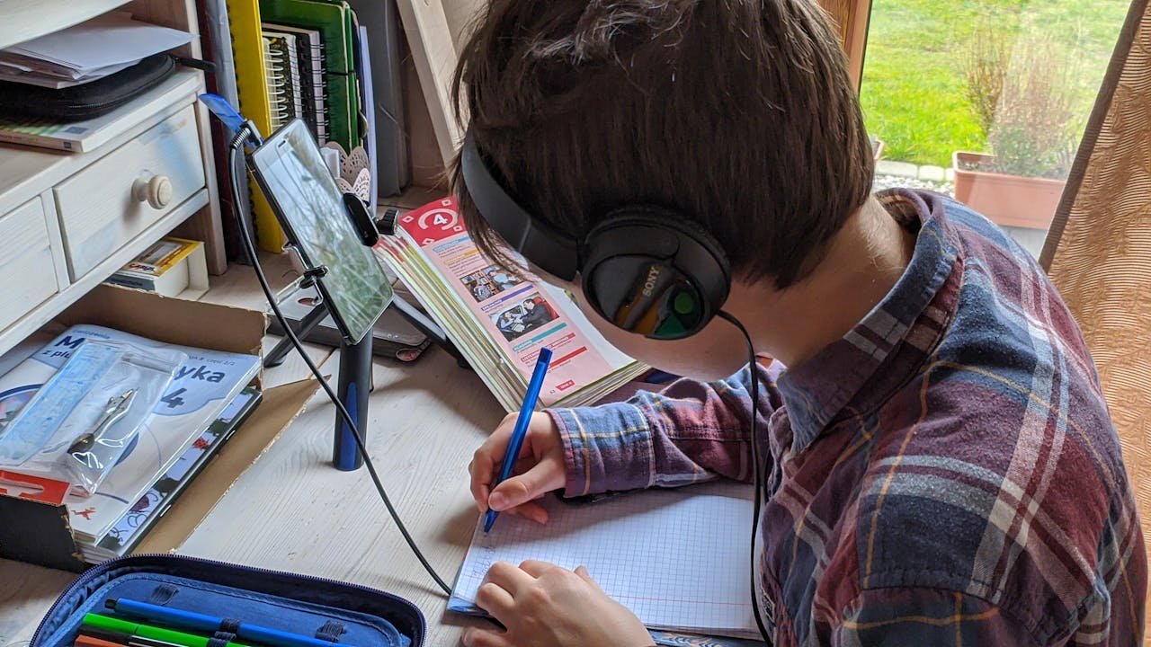 Home Young boy writing notes during an online class at home, focused on studying.